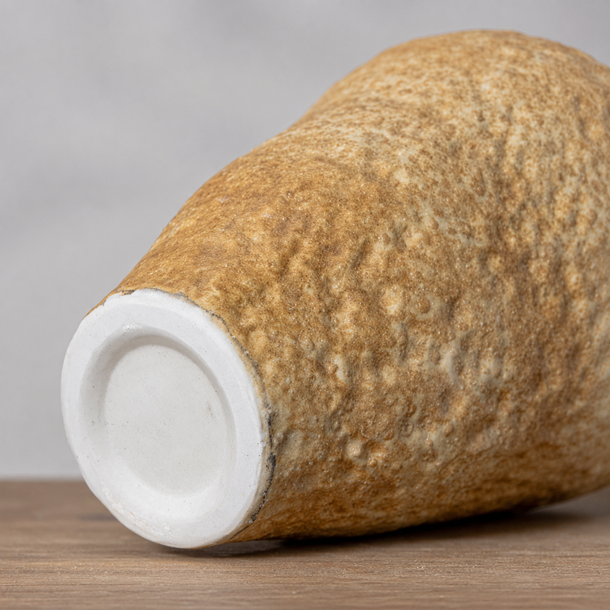 Beige ceramic vase shown on its side with polished white base