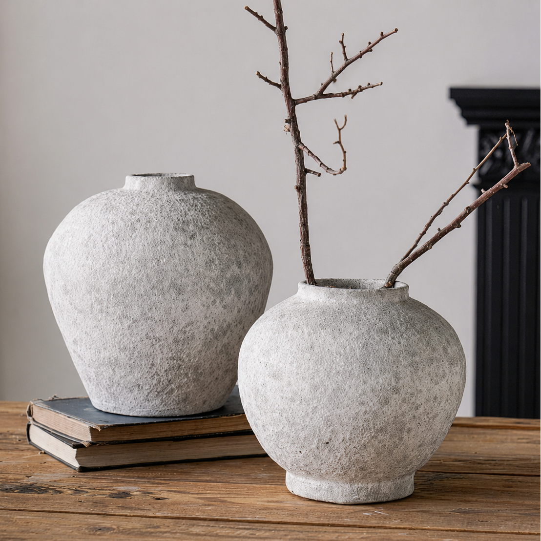 Two textured ceramic vases with branches styled on books and wooden table