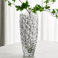 Clear bubble textured glass vase holding green leafy branches on a white table