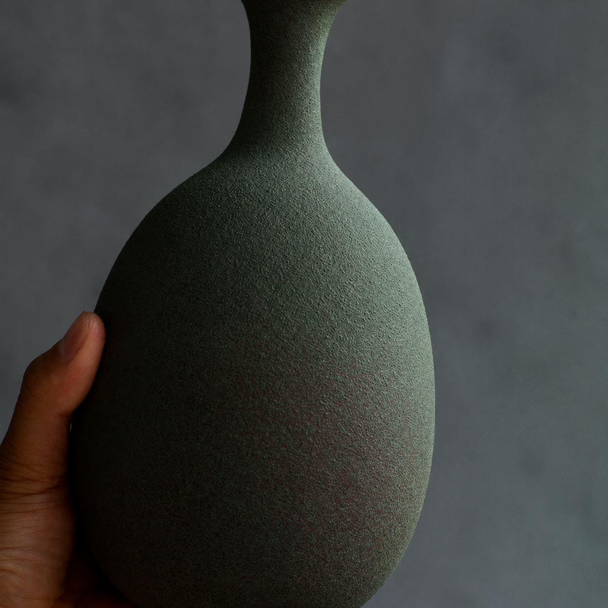 Close up of rounded body and slender neck on green ceramic vase