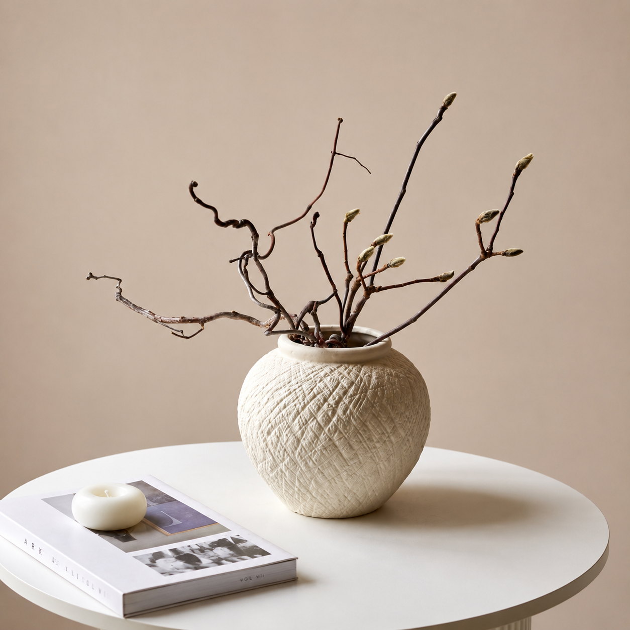 Round ivory textured ceramic vase styled with branches on a white coffee table