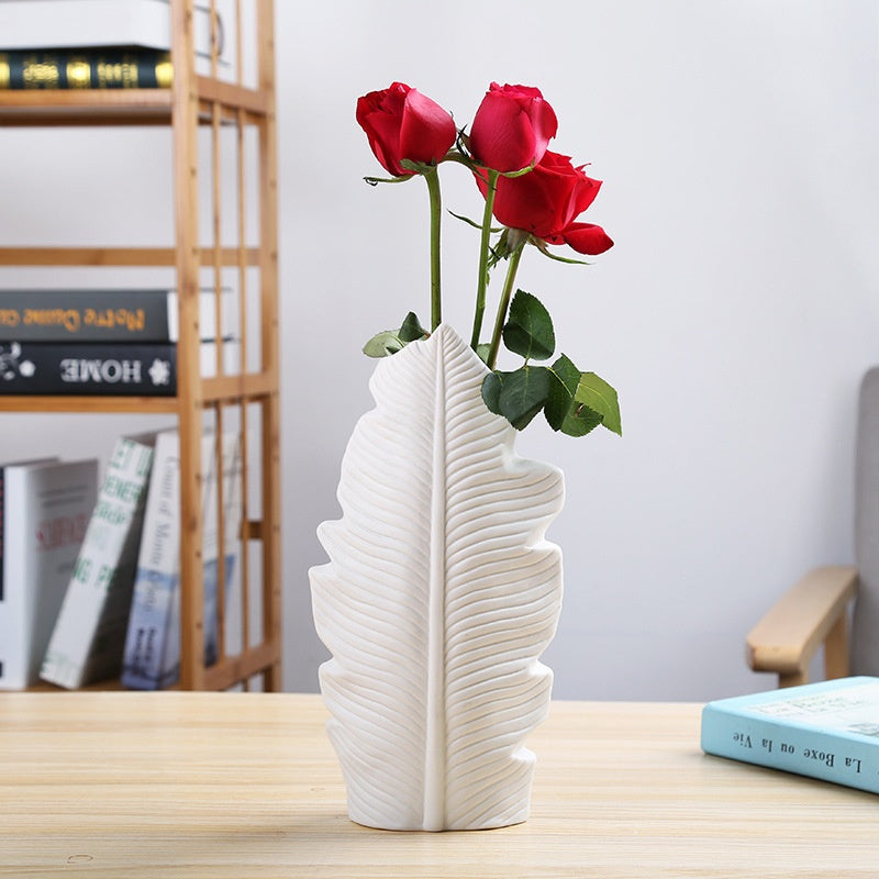 White ceramic leaf vase with red roses on a modern wooden table