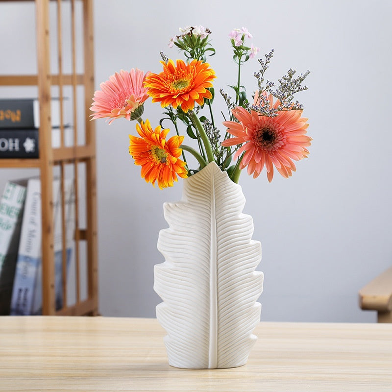 Textured white ceramic leaf vase with bright flowers in a minimalist room