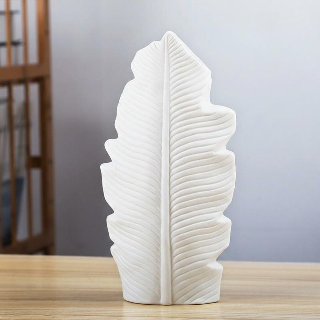 Large white ceramic leaf vase with ribbed botanical texture on a tabletop