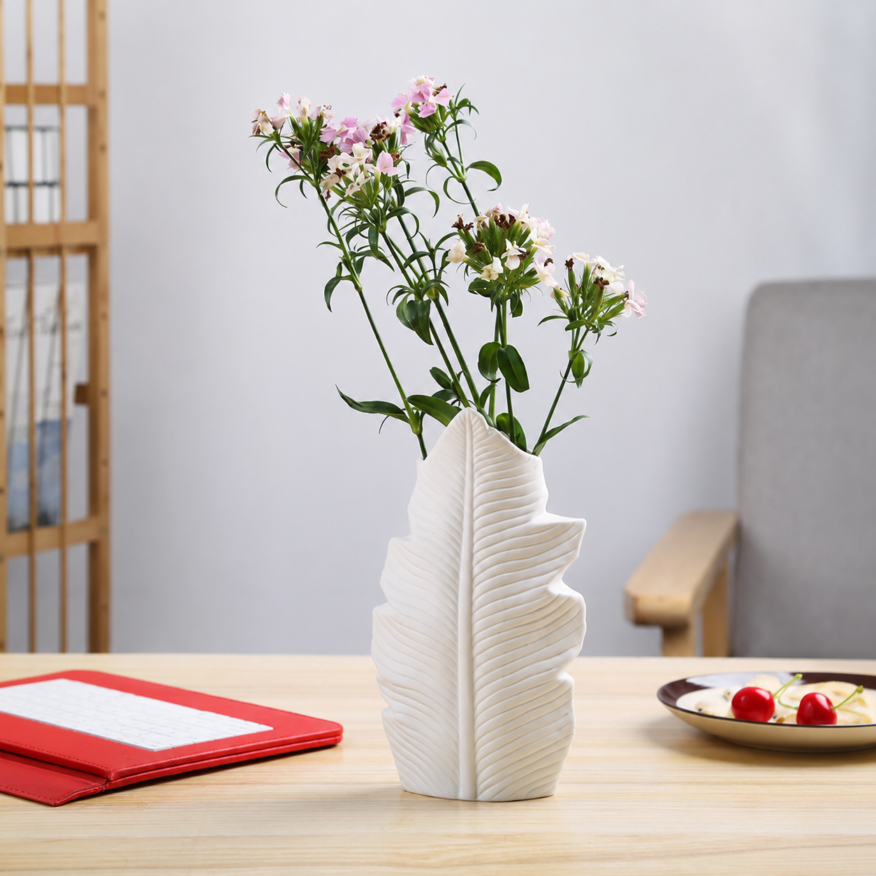 White ceramic leaf vase with flowers styled beside a notebook and plate
