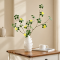 White ceramic leaf vase with yellow flowers on a wooden side table