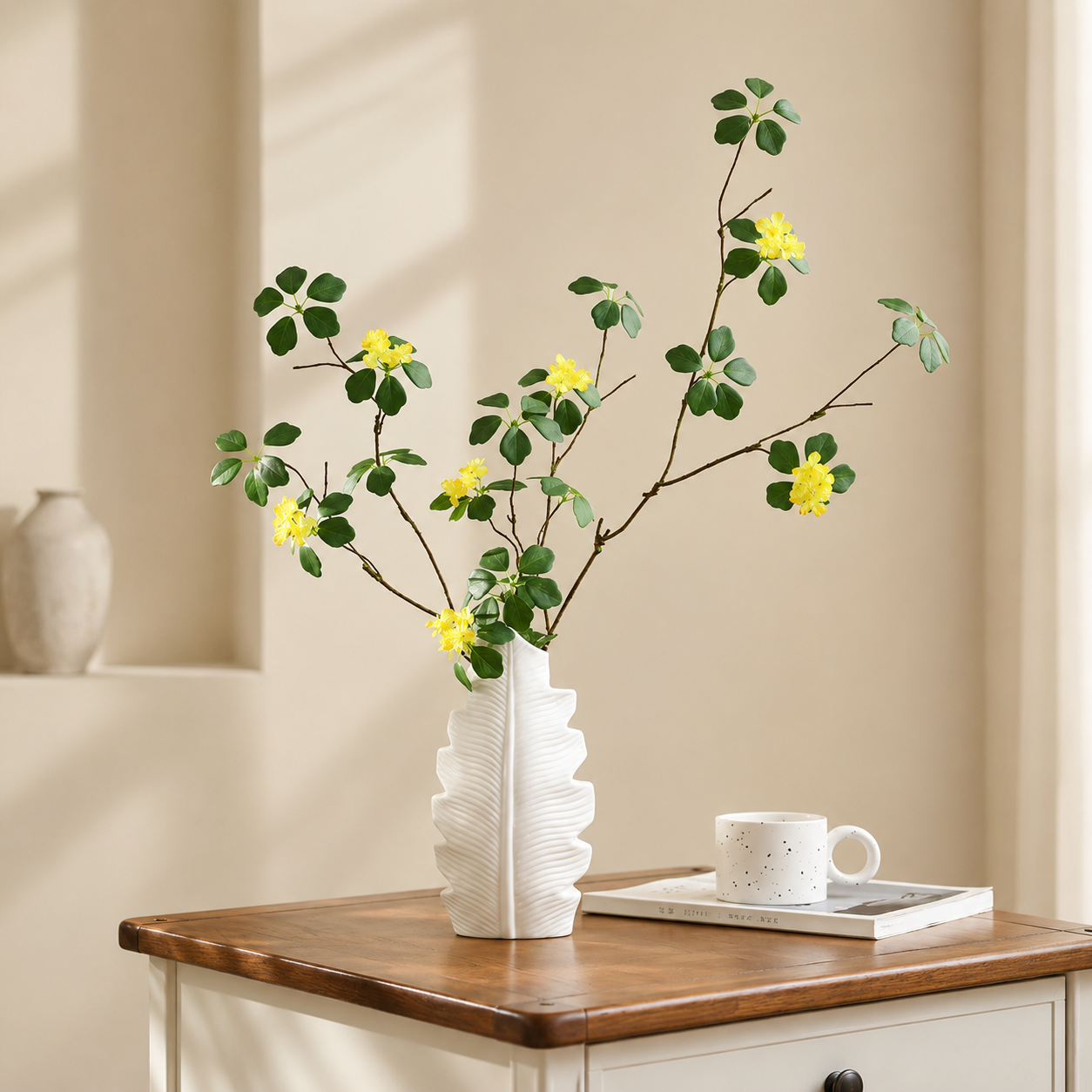 White ceramic leaf vase with yellow flowers on a wooden side table