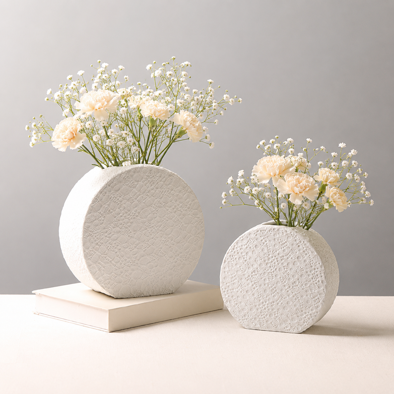 Textured white ceramic round vases with cream flowers on a book