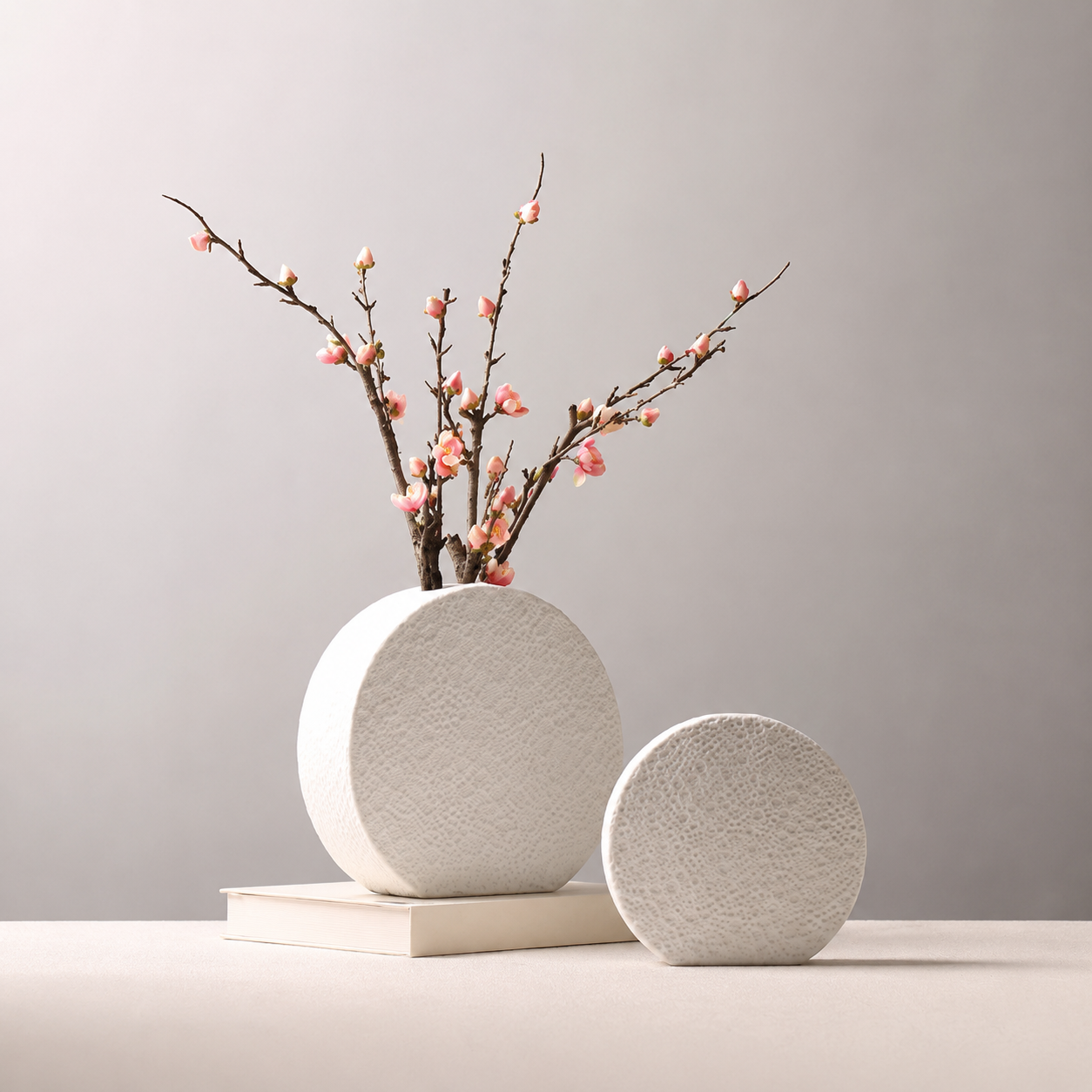 Large textured white ceramic round vase with pink blossom branches and medium vase beside it