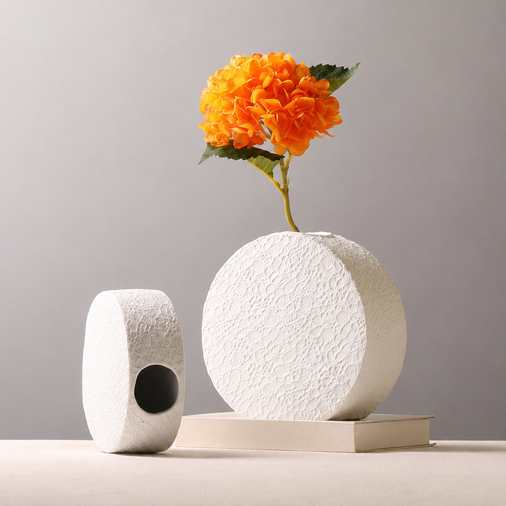Large textured white ceramic round vase with orange flower and small vase beside it