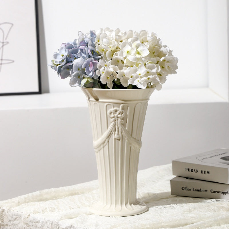 White ceramic Rosette vase with blue hydrangeas on stacked books