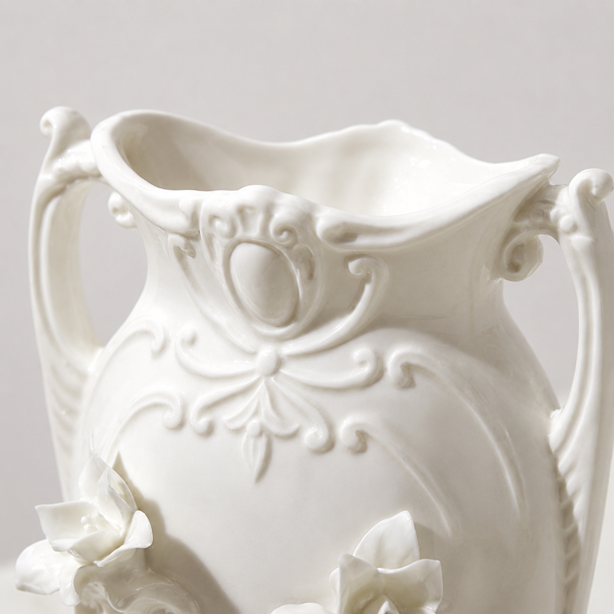 Close-up of scalloped rim and ornate handles on white ceramic floral vase