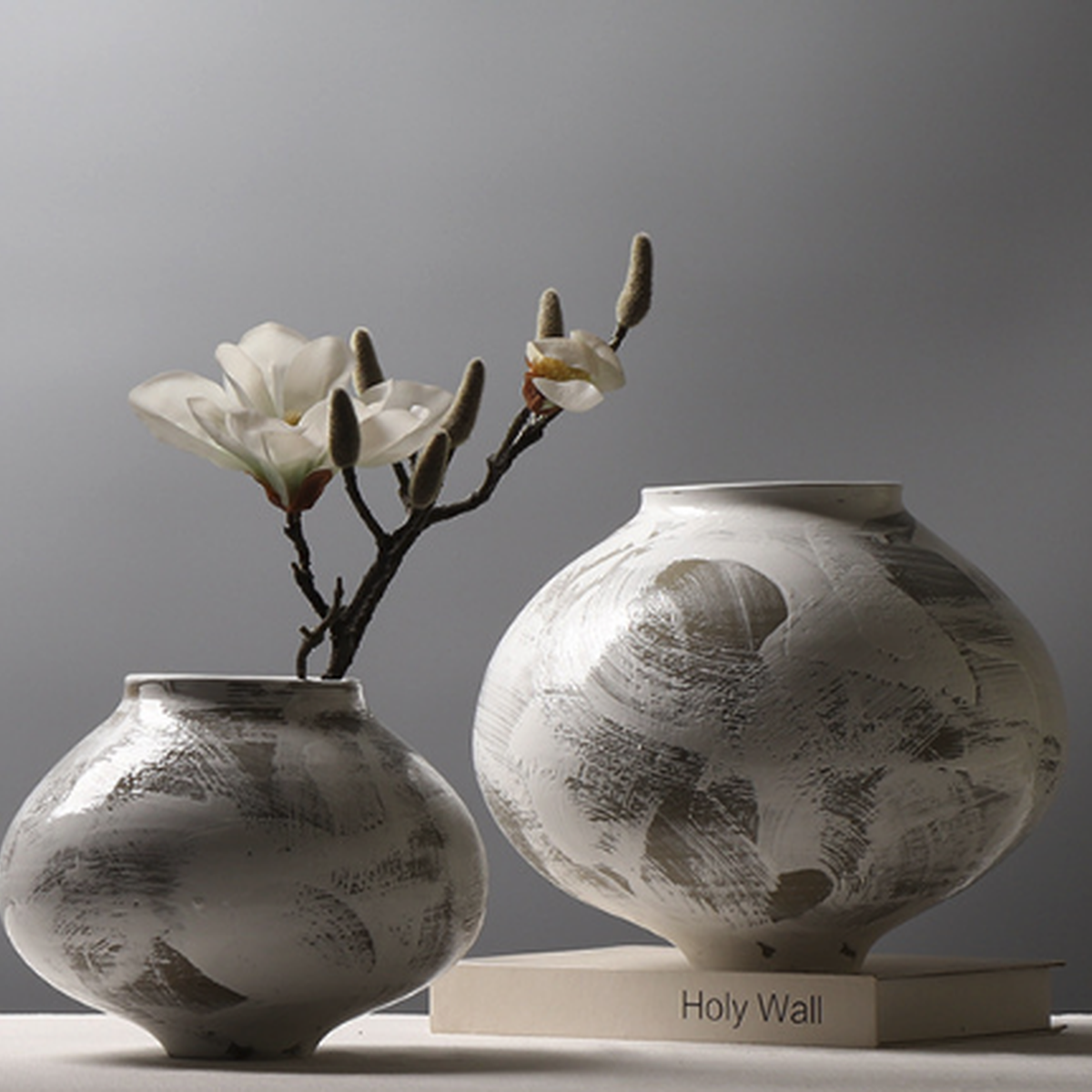 Two ceramic brushstroke vases styled with white floral branches on neutral background
