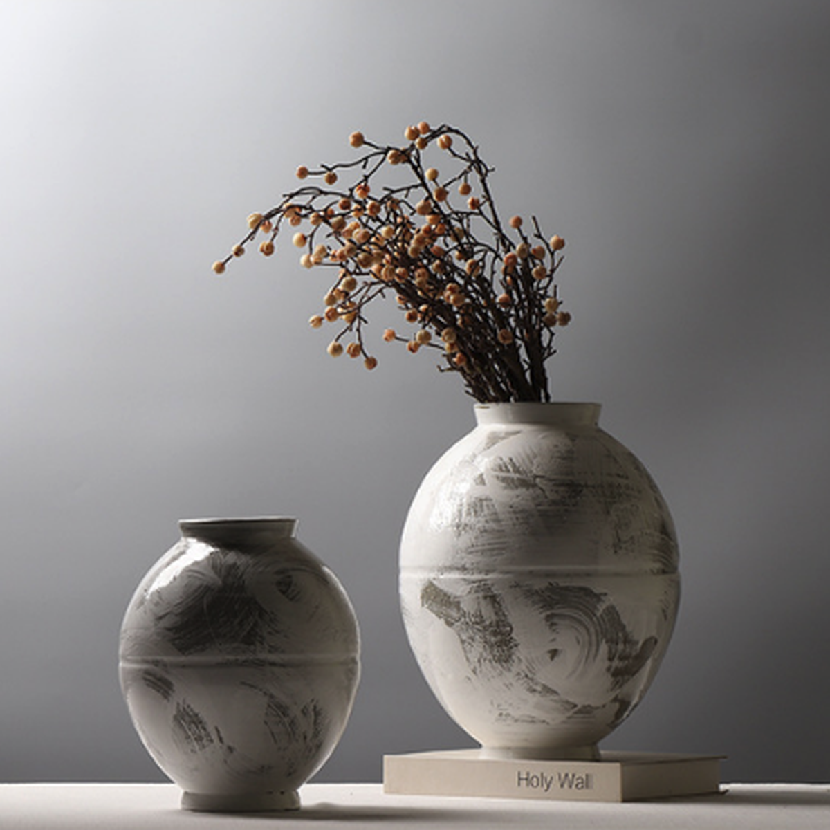 Two ceramic brushstroke vases styled with orange berry branches on stacked books