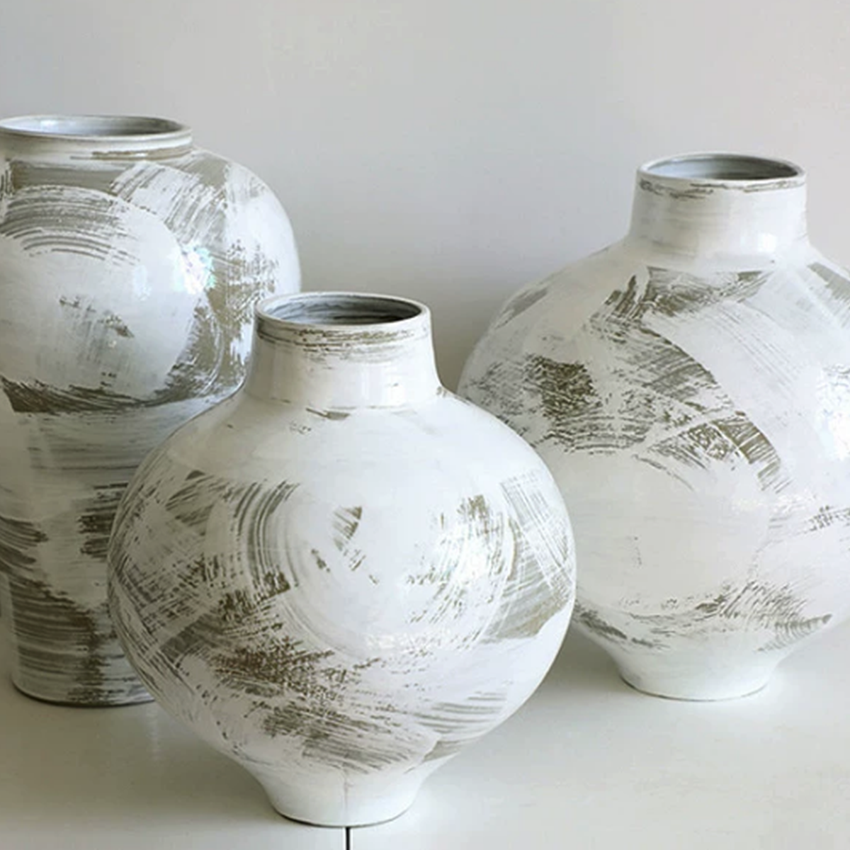 Three white and neutral ceramic vases with abstract brushstroke pattern on white surface
