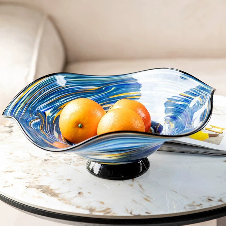 Blue wavy art glass centerpiece bowl filled with oranges on marble table