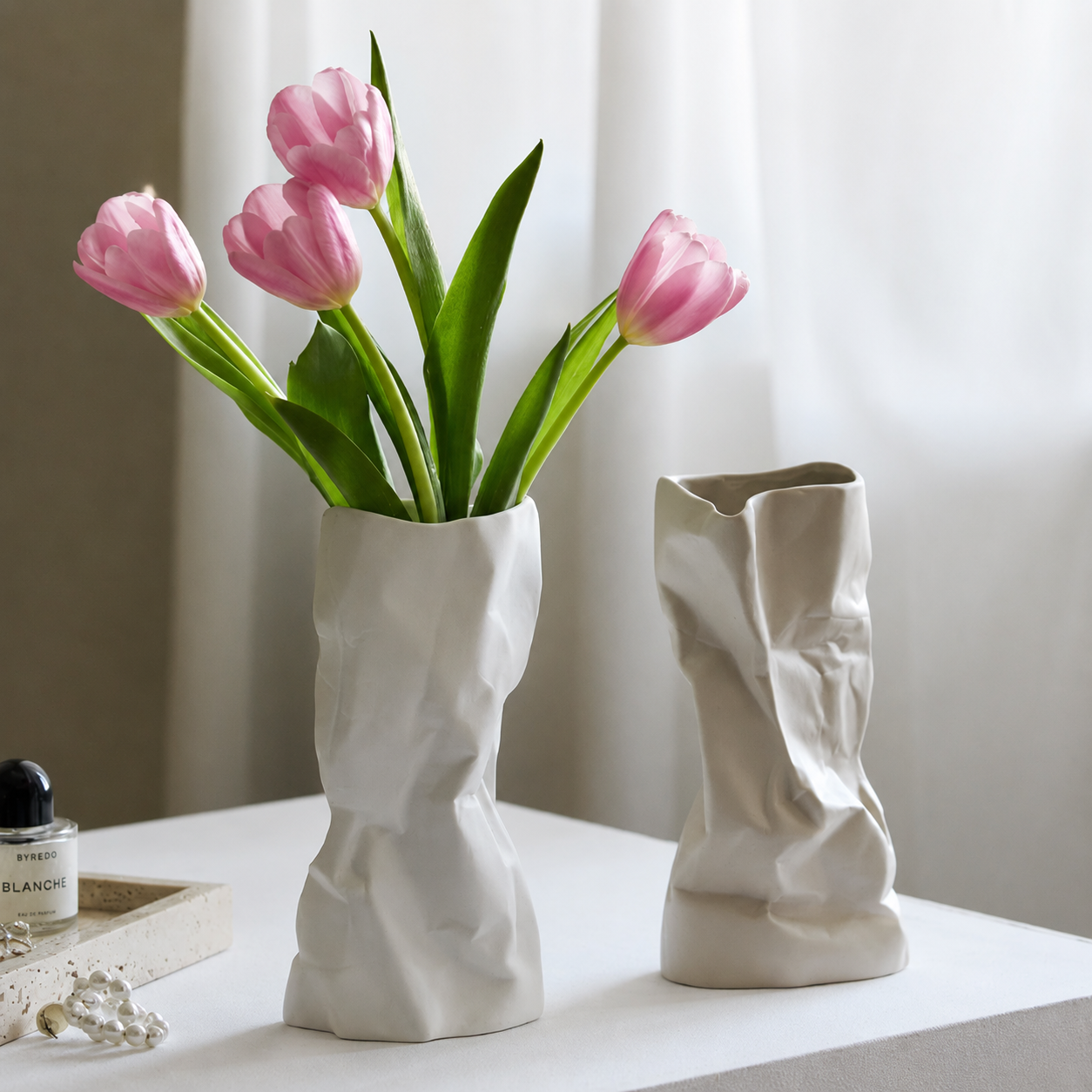 White ceramic crumpled vase with pink tulips beside a smaller vase