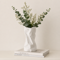 White ceramic crumpled vase with eucalyptus stems on stacked books