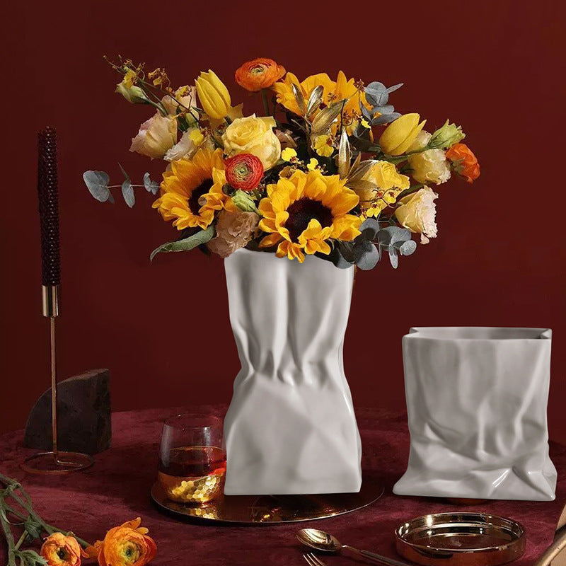 White ceramic crumpled paper bag vase with a colorful floral arrangement and matching smaller vase