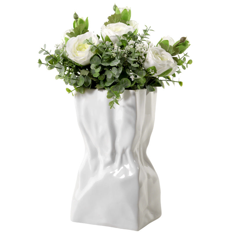 White ceramic crumpled vase with white flowers on a white background