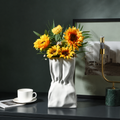 White ceramic crumpled vase with sunflowers on a dark tabletop
