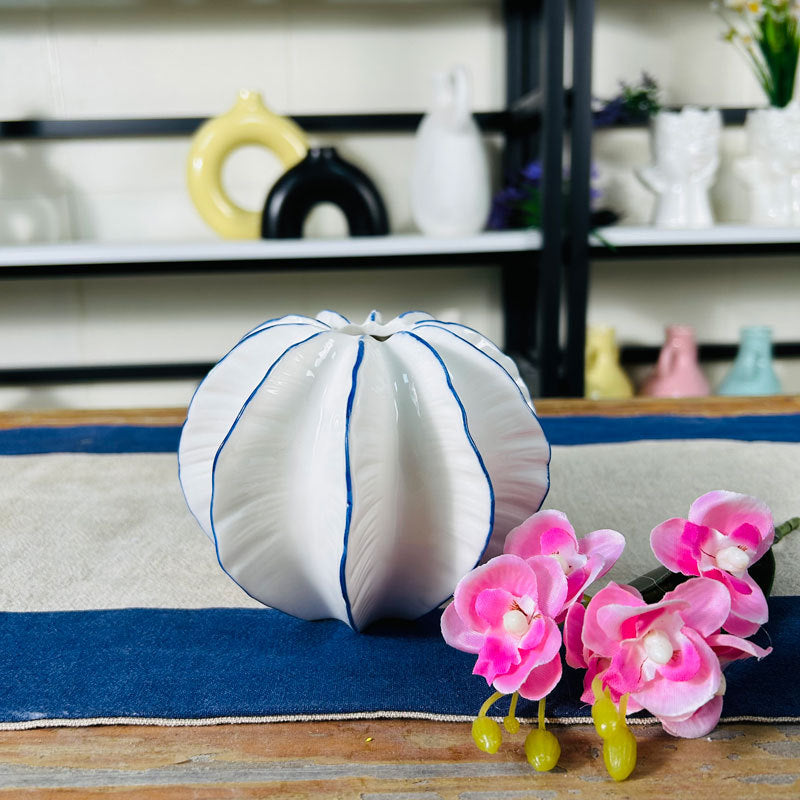 Short white ceramic petal vase with blue trim styled on a blue table with pink flowers