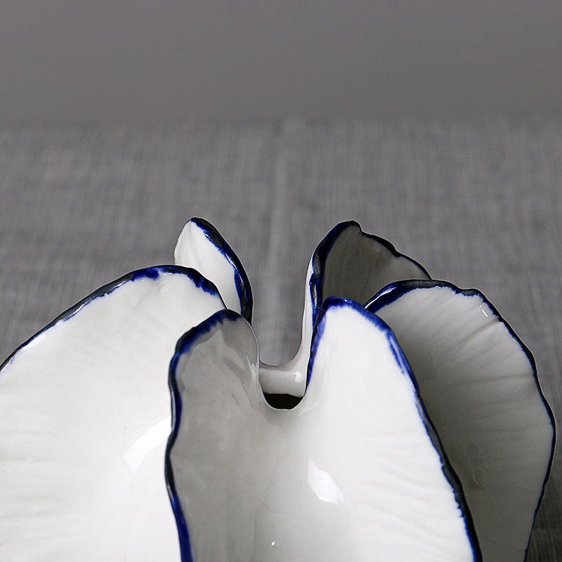 Close-up of short white ceramic petal vase with blue trim and sculptural opening