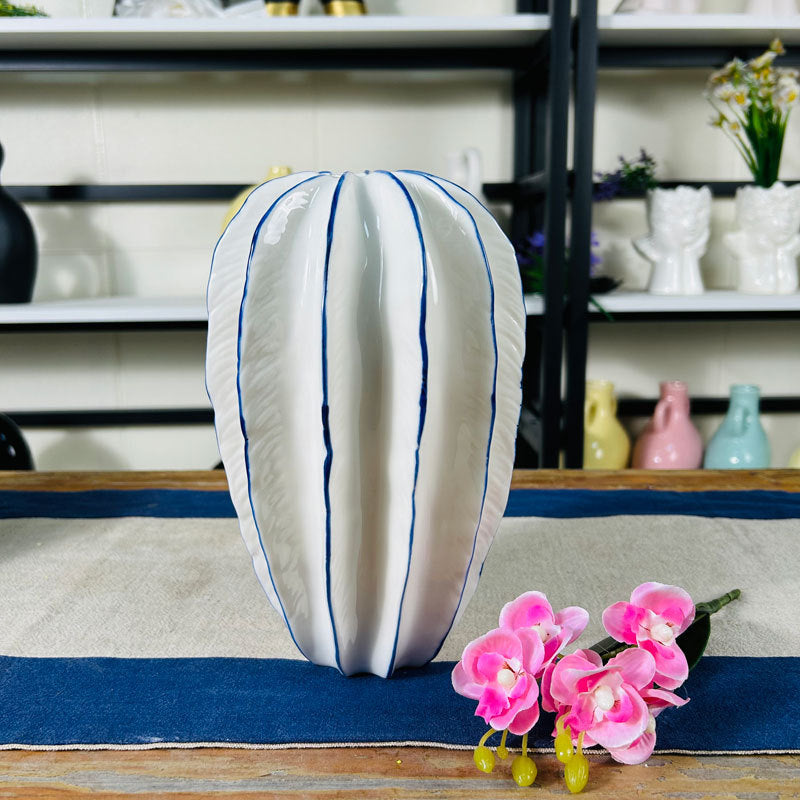 Tall white ceramic petal vase with blue trim styled on a blue table