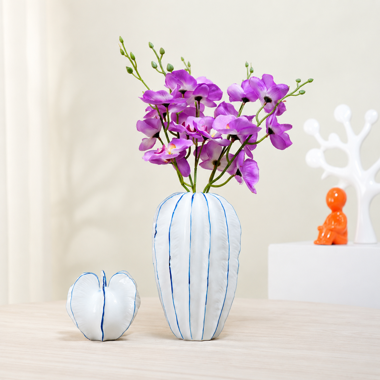 White ceramic petal vase with blue trim and purple flowers on a light wood table