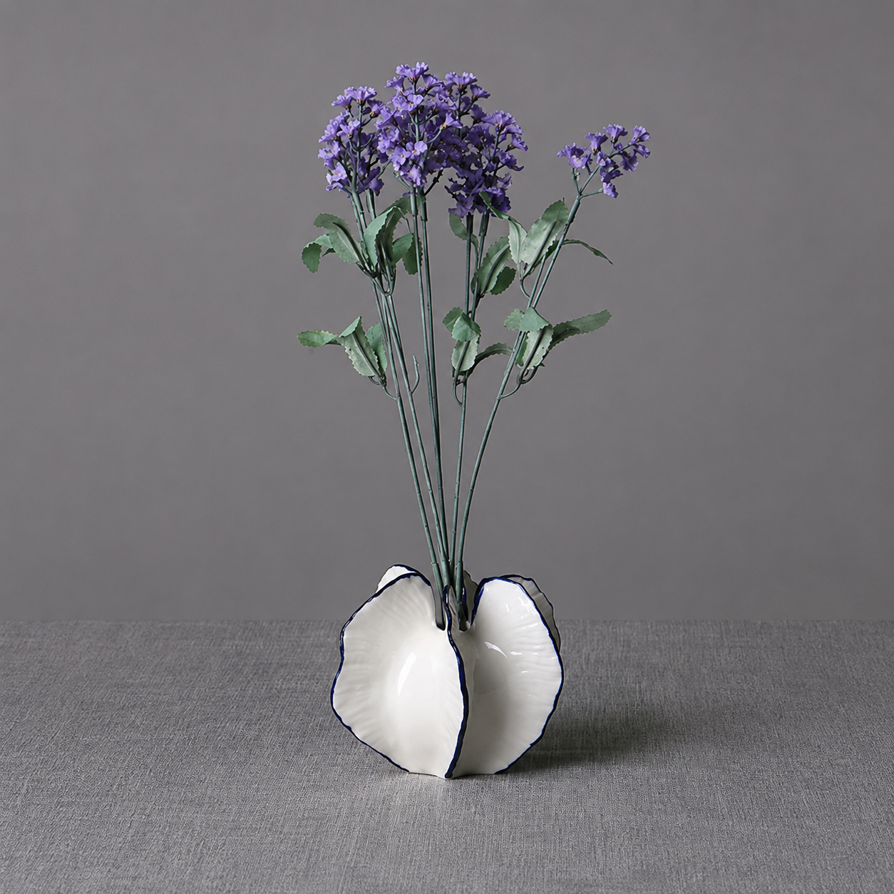 Short white ceramic petal vase with purple flowers on a gray background