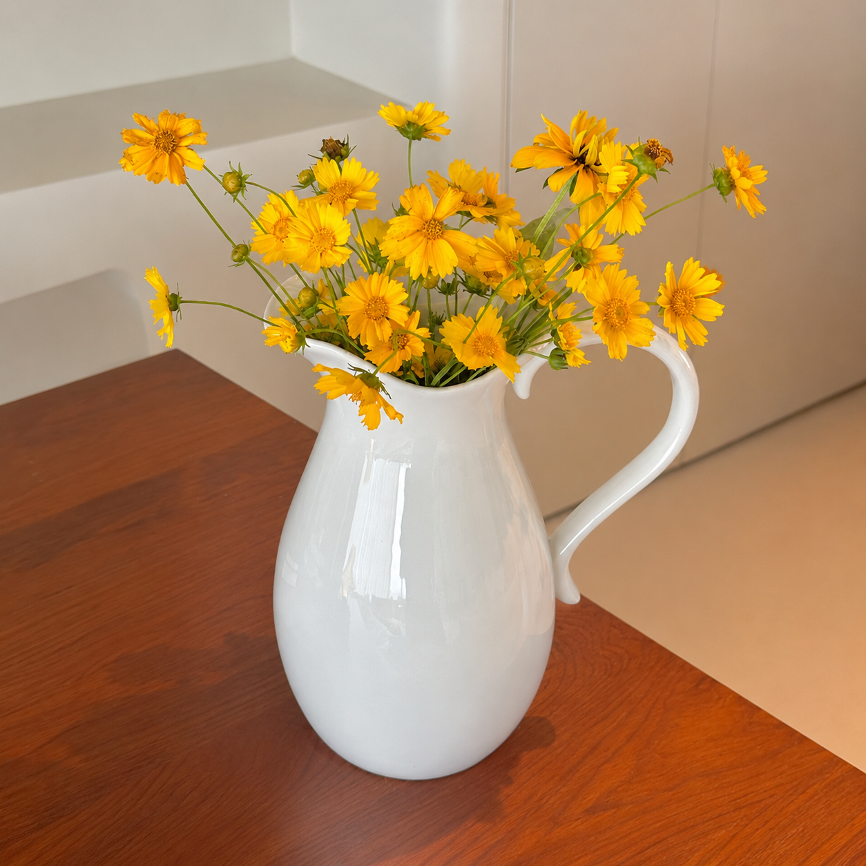 White ceramic pitcher vase with yellow flowers on wooden table