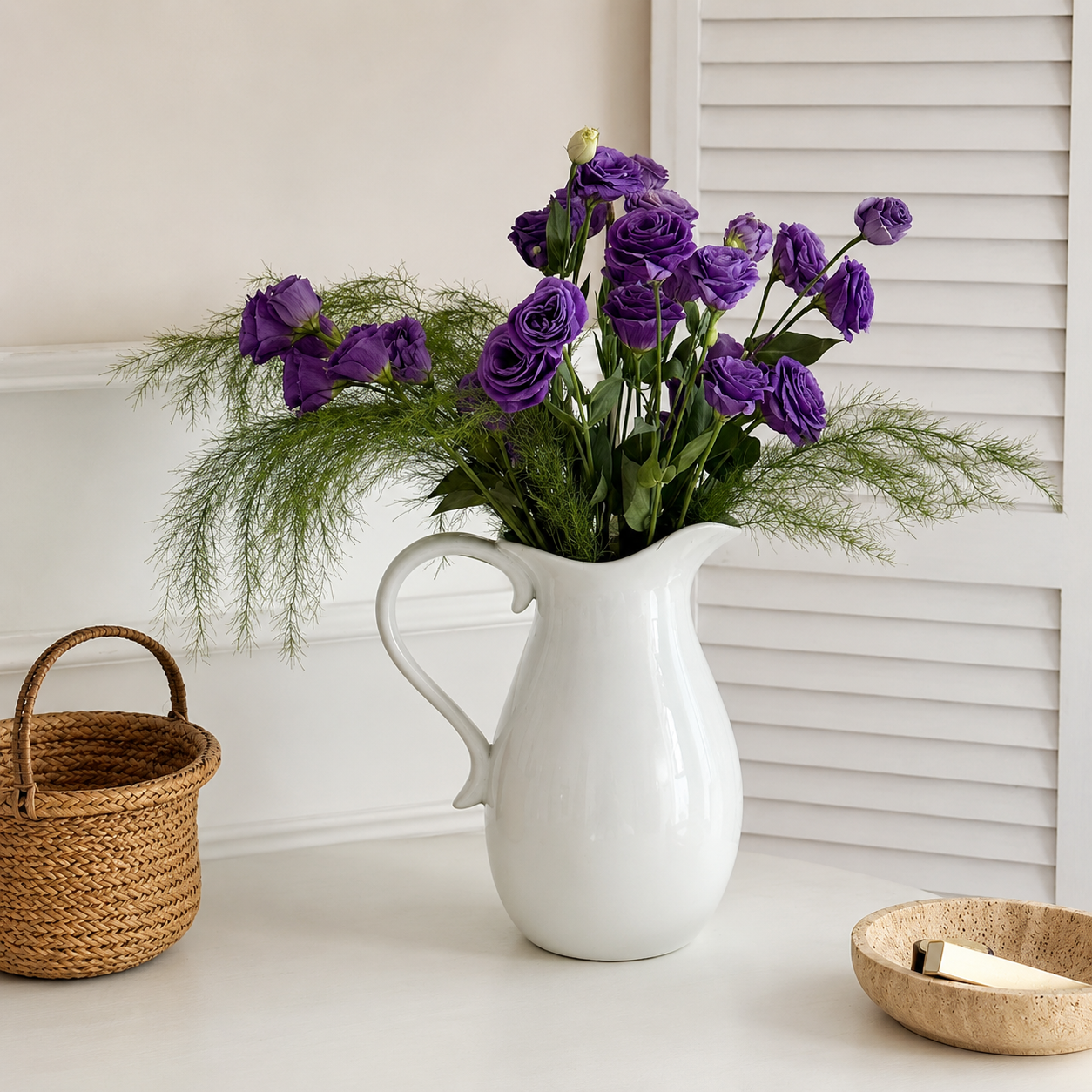 White ceramic pitcher vase with purple flowers and greenery on white tabletop