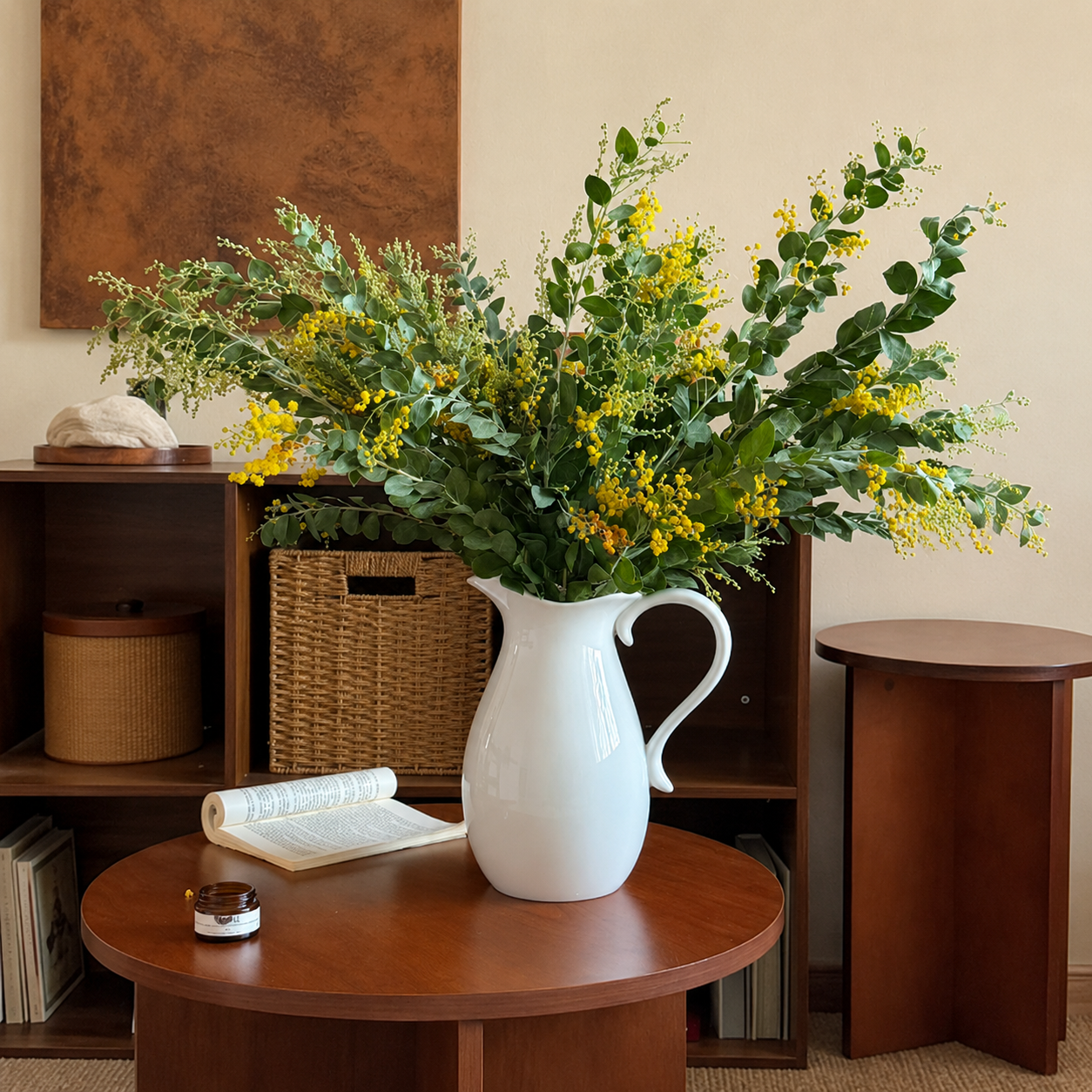 White ceramic pitcher vase with large greenery and yellow floral arrangement on round table