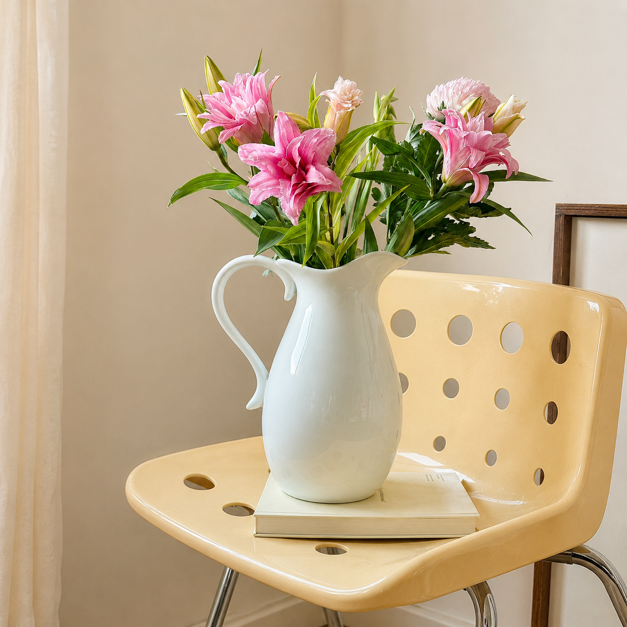 White ceramic pitcher vase with pink flowers styled on cream chair
