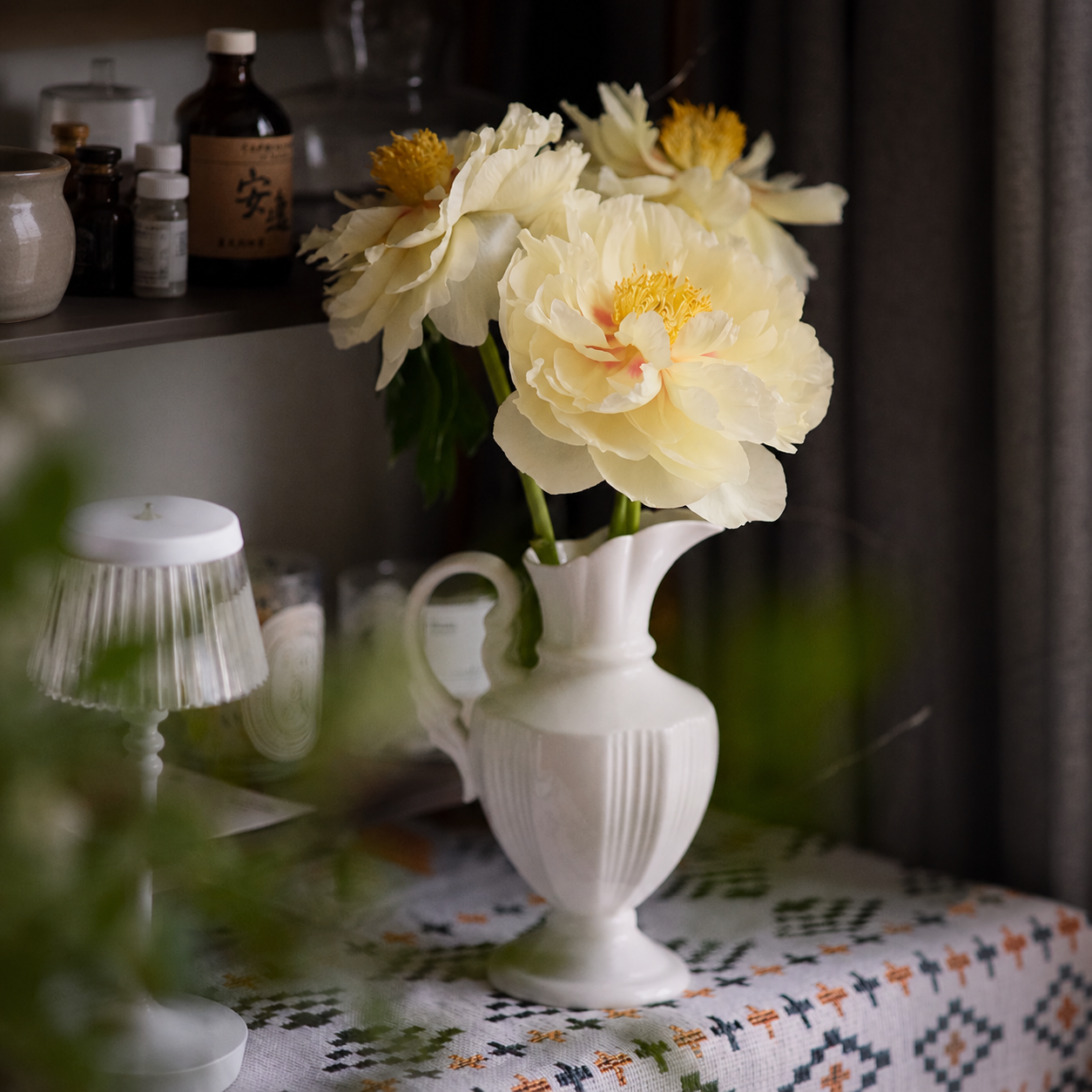 White ceramic pitcher vase with cream flowers in cozy vintage interior