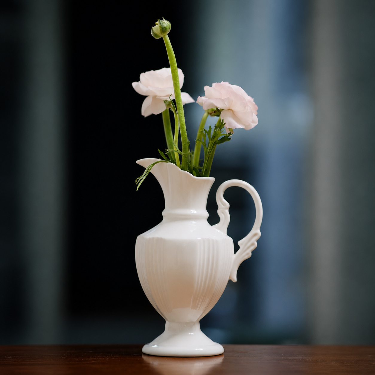 White ceramic pitcher vase with pale pink flowers on wooden table