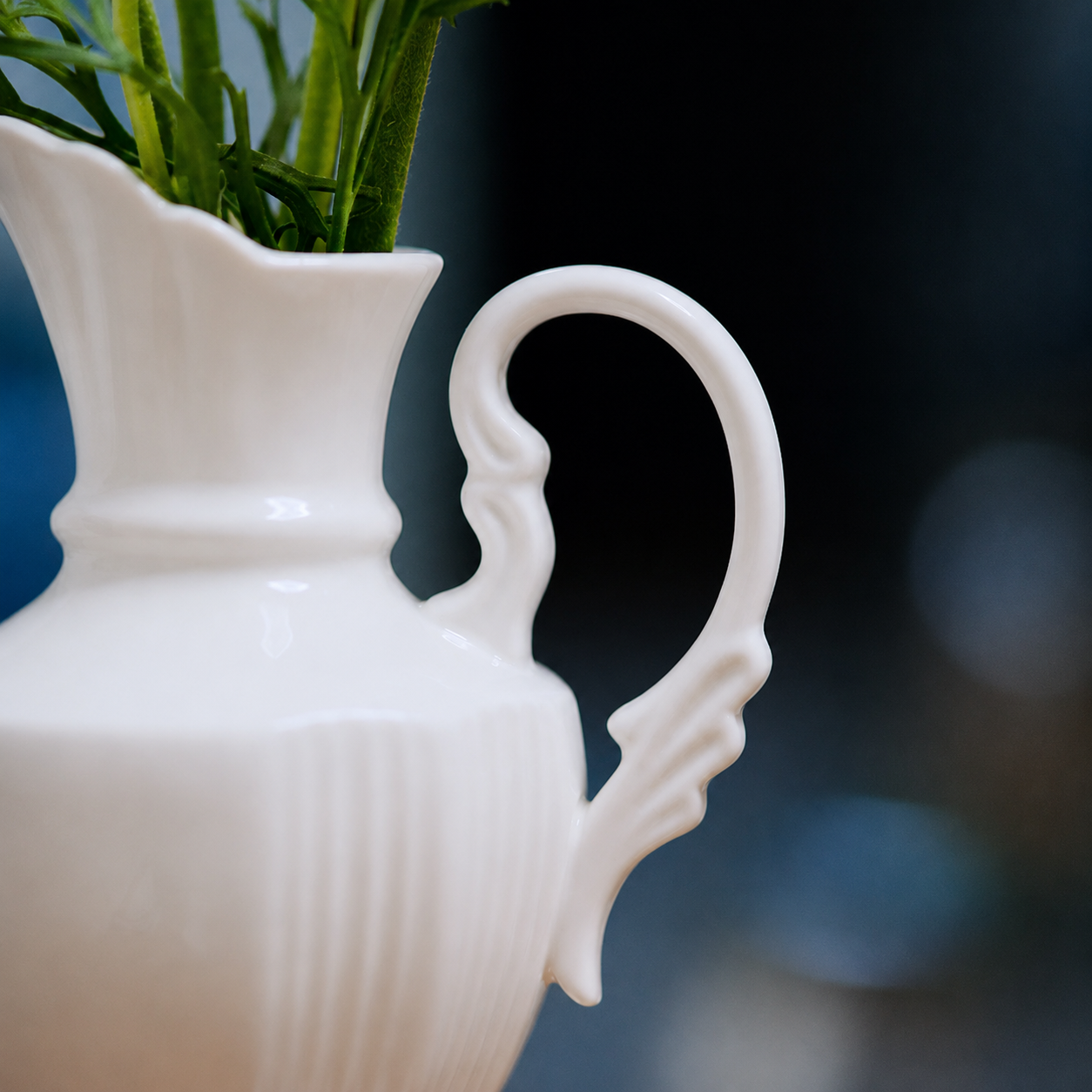 Close-up of curved handle on glossy white ceramic pitcher vase