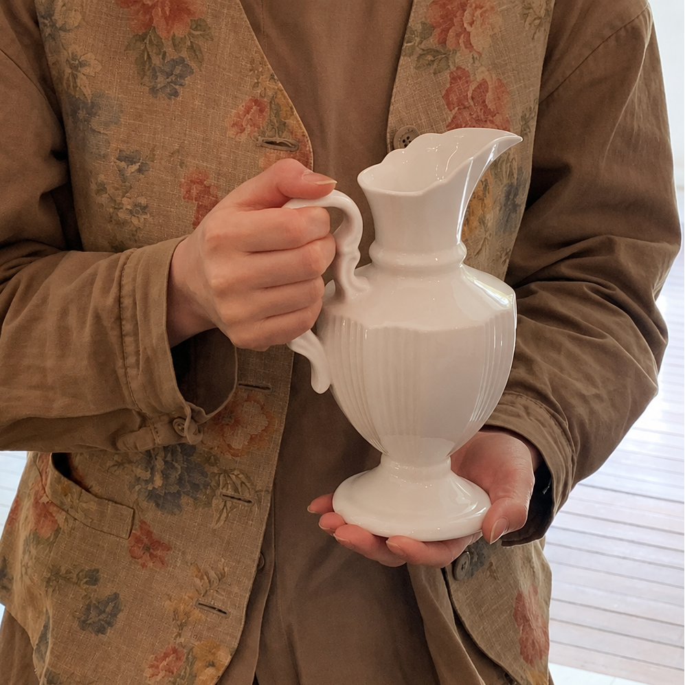White ceramic pitcher vase held by hand showing size, handle, and pedestal base