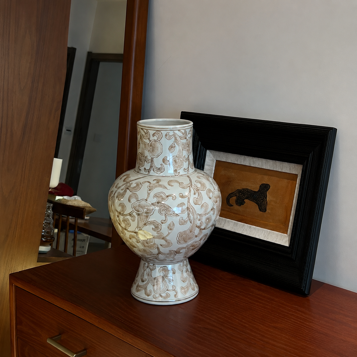 Close-up of white and gold floral ceramic vase on wooden dresser with framed art for classic interior styling