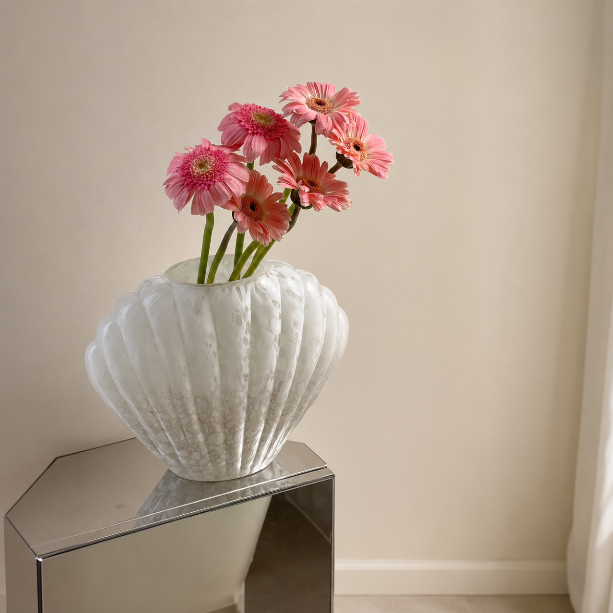 Large white shell-shaped glass vase with pink flowers on mirrored side table in minimalist corner