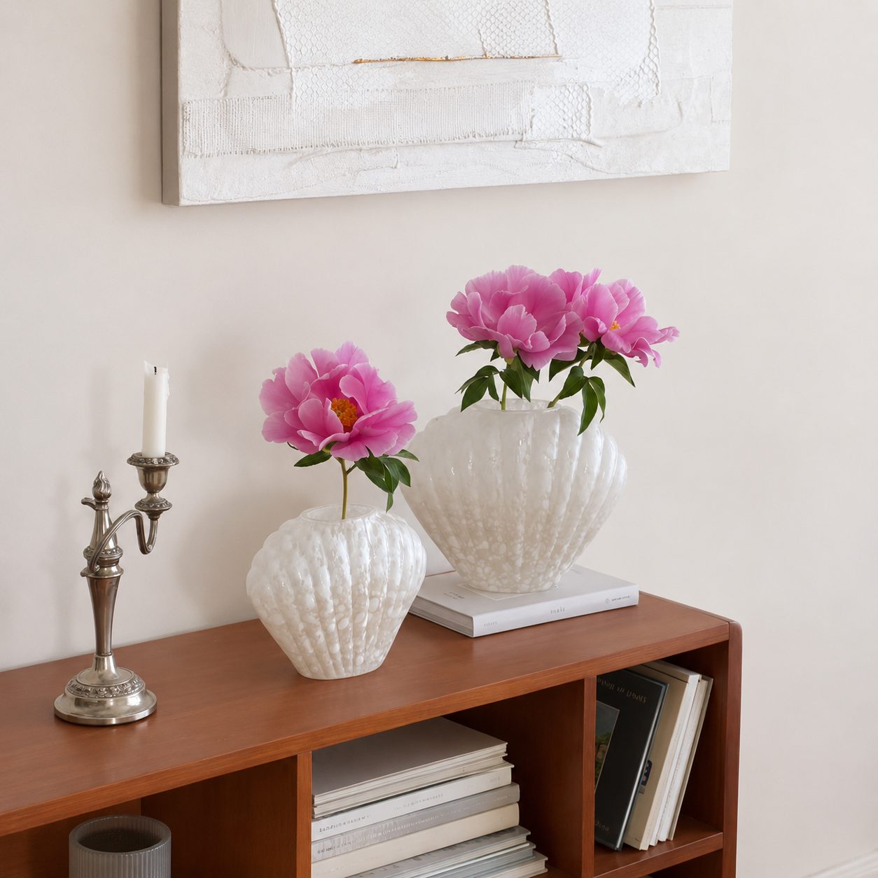 Medium and Large white shell-shaped glass vases with pink flowers on wooden console table