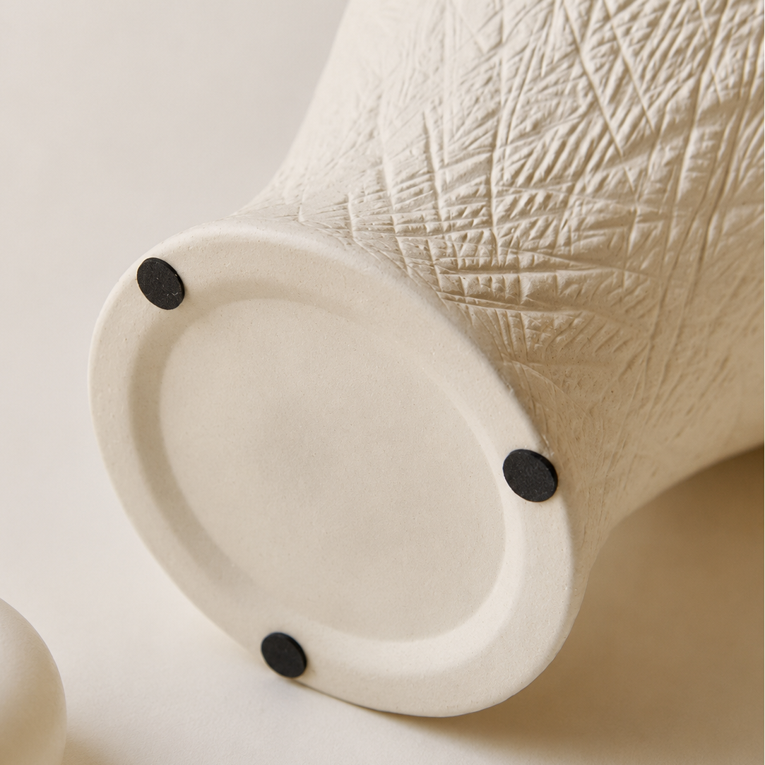 Close up of ivory ceramic vase base with protective pads and textured carved surface