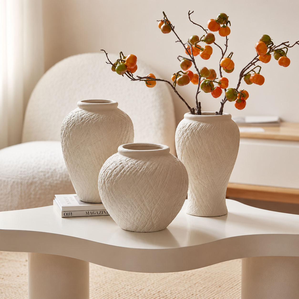 Ivory textured ceramic vases styled with orange berry branches on a modern white coffee table