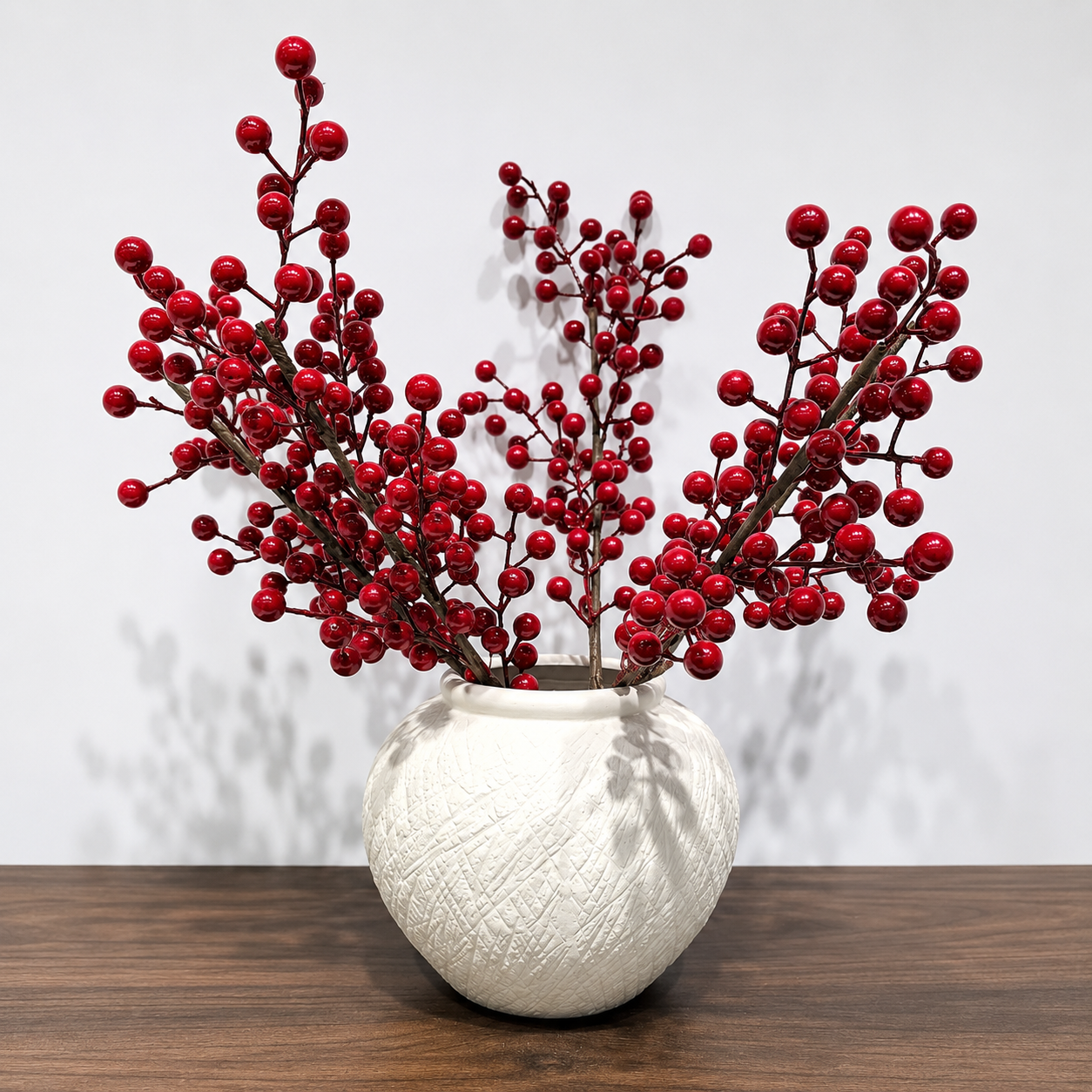 Round ivory textured ceramic vase styled with red berry branches on a wooden table