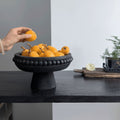 Matte black wooden beaded pedestal centerpiece bowl filled with oranges on dining table