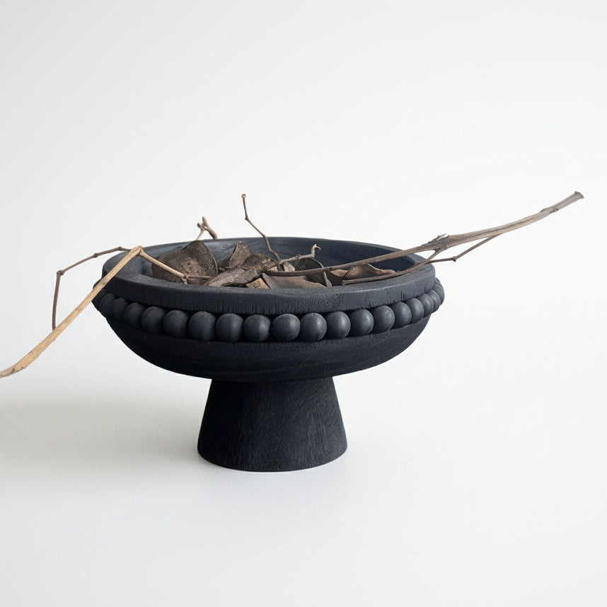 Black wooden beaded pedestal bowl styled with decorative branches on white background