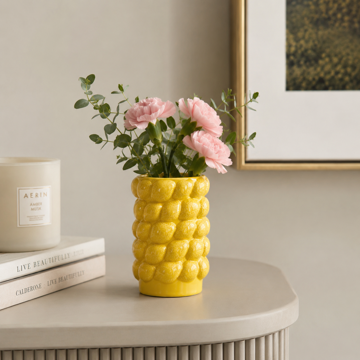 Small yellow ceramic lemon textured vase with pink flowers on a round side table