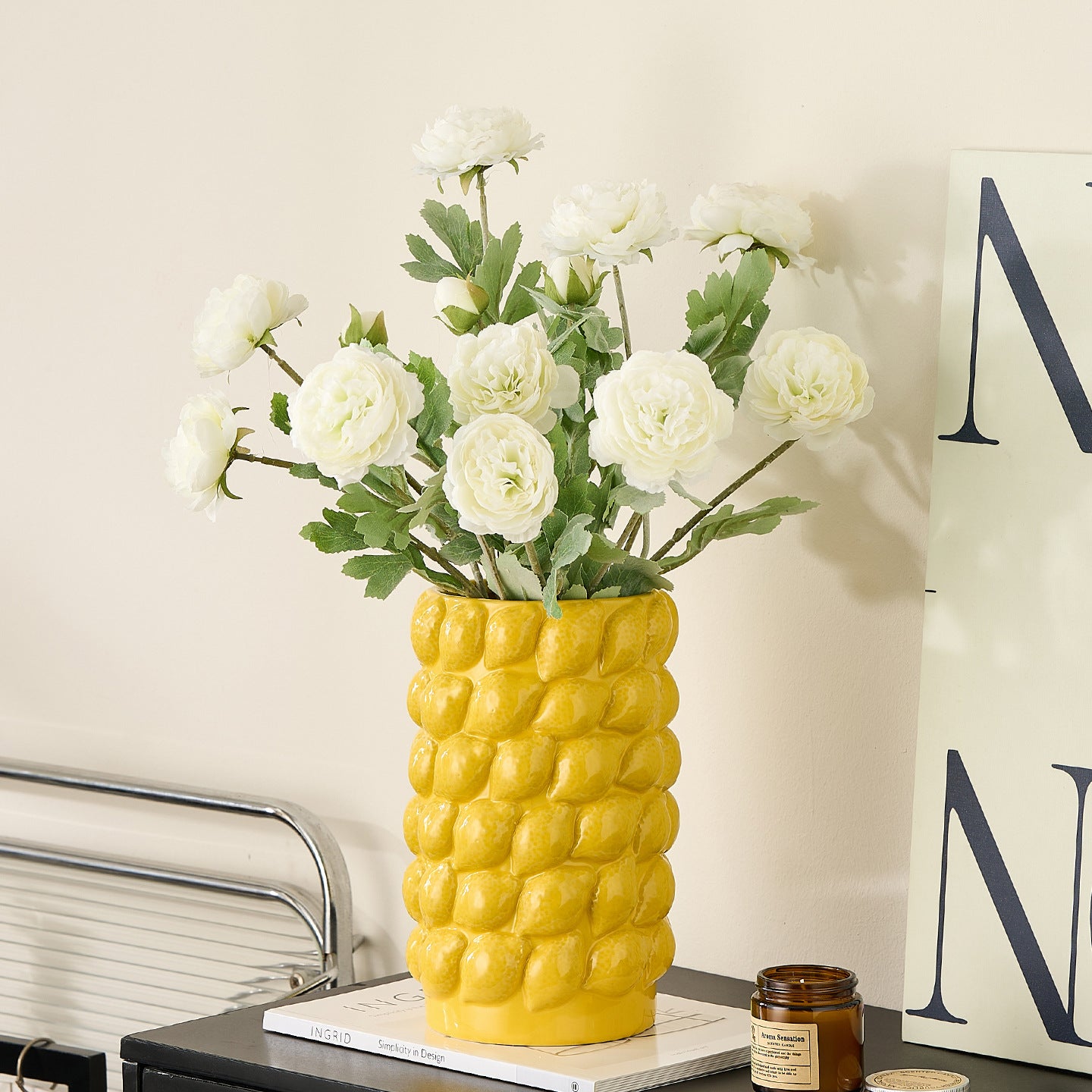 Large yellow ceramic lemon textured vase with white floral arrangement on a modern shelf