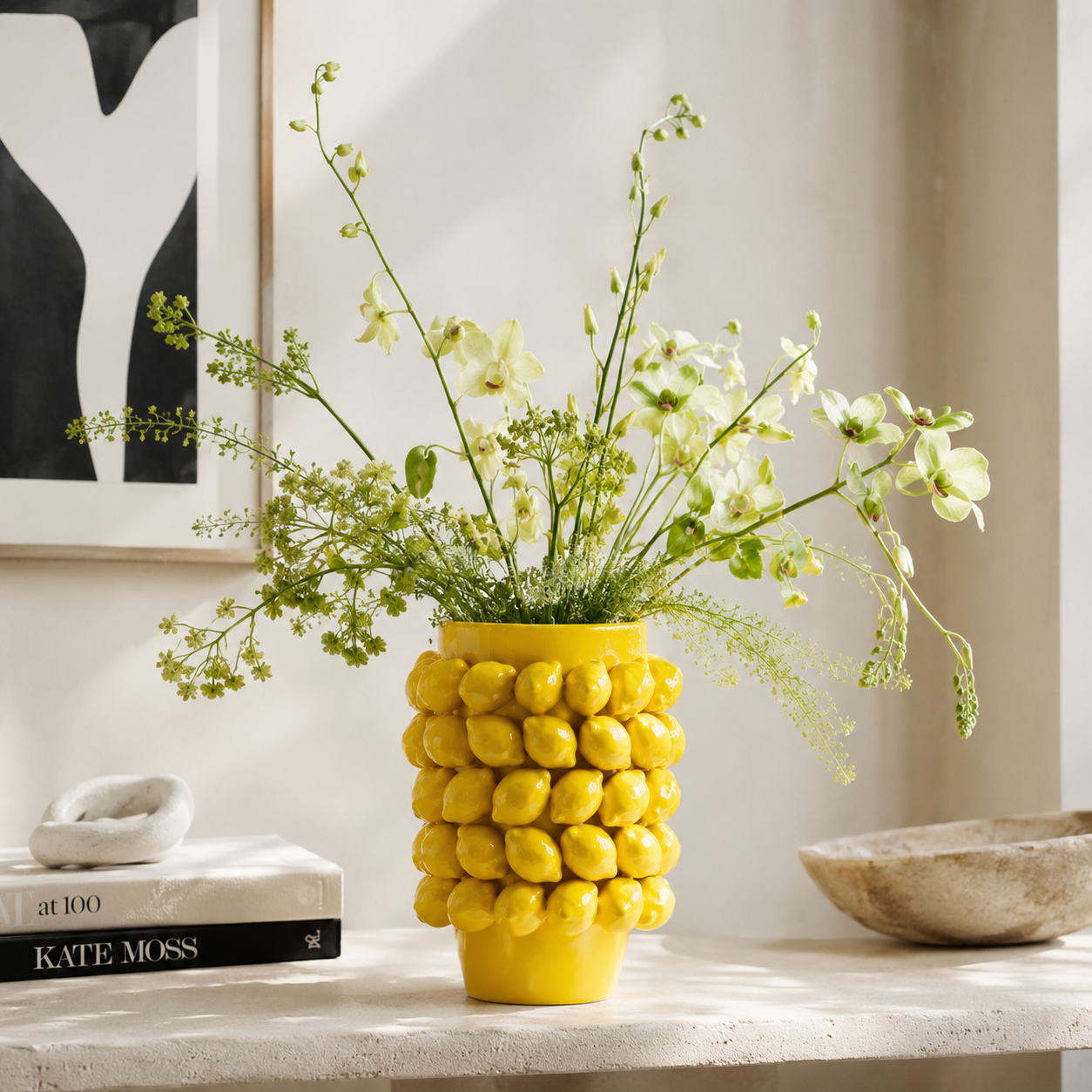 Yellow glazed ceramic lemon vase with airy green botanical stems on a contemporary console table