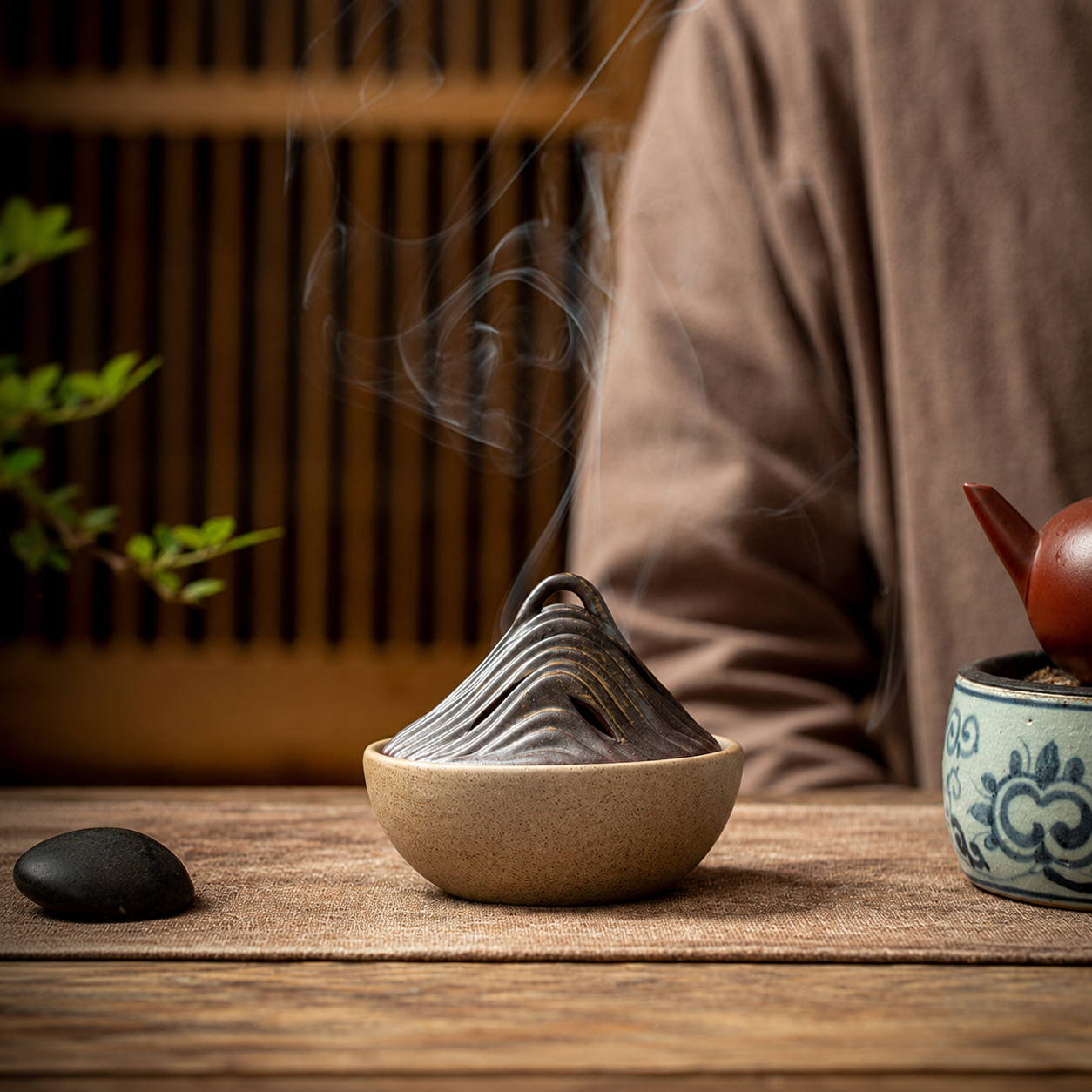 Ceramic mountain incense burner with smoke beside teapot in calm tea ritual setting